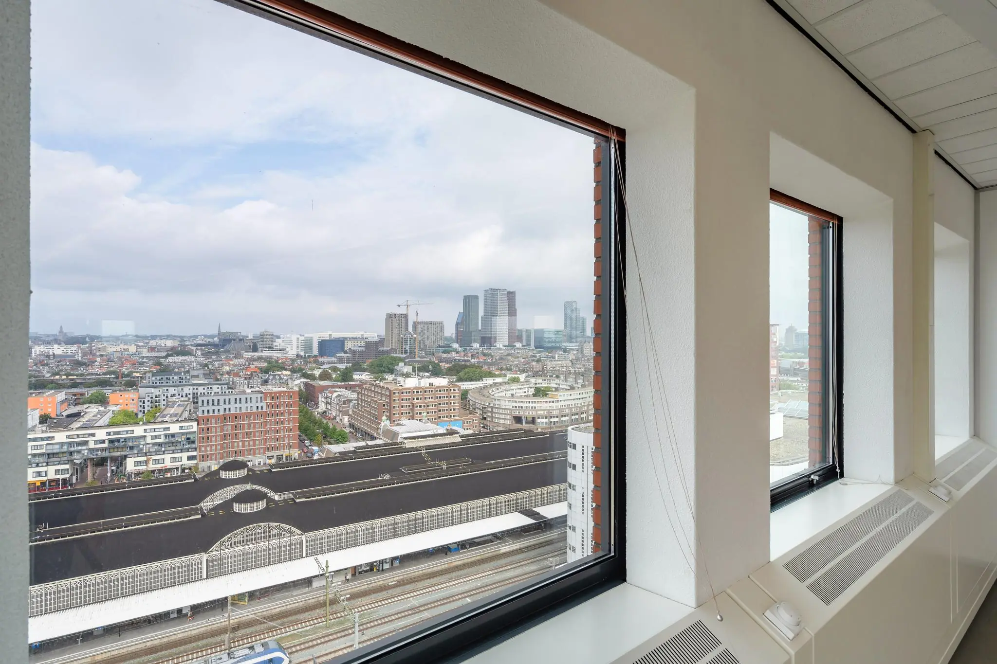 Uitzicht vanuit een raam op het Johanna Westerdijkplein in Den Haag met zicht op het station en de skyline van de stad.